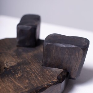 Puede incluir: Una bandeja de madera tallada a mano, de color marr&oacute;n oscuro, con tres patas cuadradas en forma de bloques. La bandeja tiene una veta de madera natural y una est&eacute;tica r&uacute;stica y org&aacute;nica. Las patas est&aacute;n unidas a la base de la bandeja.