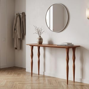 Peut inclure: Une console en bois dotée de quatre pieds sculptés et facettés ainsi qu'un plateau rectangulaire. La table supporte un vase en céramique avec des branches nues et deux livres empilés. Un miroir rond à cadre fin est fixé au mur au-dessus.