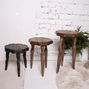 May include: Three wooden stools of varying heights and shapes. The smallest is dark brown, the middle one is a lighter brown, and the tallest is a medium brown. Each stool has a unique, natural-edged top and three legs.