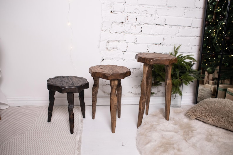 May include: Three wooden stools of varying heights and shapes. The smallest is dark brown, the middle one is a lighter brown, and the tallest is a medium brown. Each stool has a unique, natural-edged top and three legs.