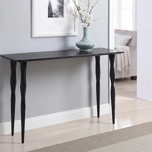 May include: A rectangular black console table featuring a smooth, flat top surface and four slender, tapered legs with a distinct faceted, geometric design. The table is constructed with a dark finish and stands on a light-coloured floor.