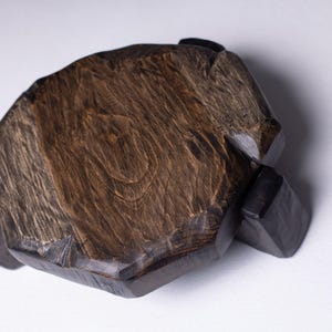 Puede incluir: Una tabla de servir de madera hecha a mano con un acabado marr&oacute;n oscuro. La tabla tiene una forma org&aacute;nica &uacute;nica y est&aacute; soportada por cuatro peque&ntilde;os pies de color oscuro. La veta de la madera es visible, lo que a&ntilde;ade encanto r&uacute;stico.