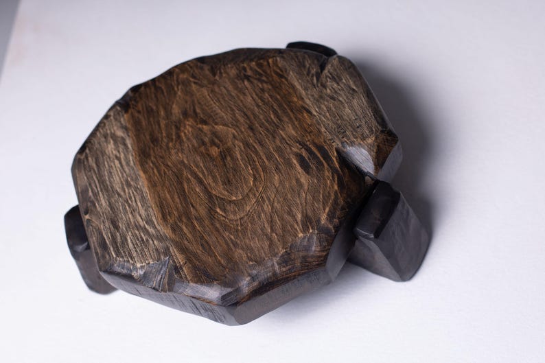 Puede incluir: Una tabla de servir de madera hecha a mano con un acabado marr&oacute;n oscuro. La tabla tiene una forma org&aacute;nica &uacute;nica y est&aacute; soportada por cuatro peque&ntilde;os pies de color oscuro. La veta de la madera es visible, lo que a&ntilde;ade encanto r&uacute;stico.