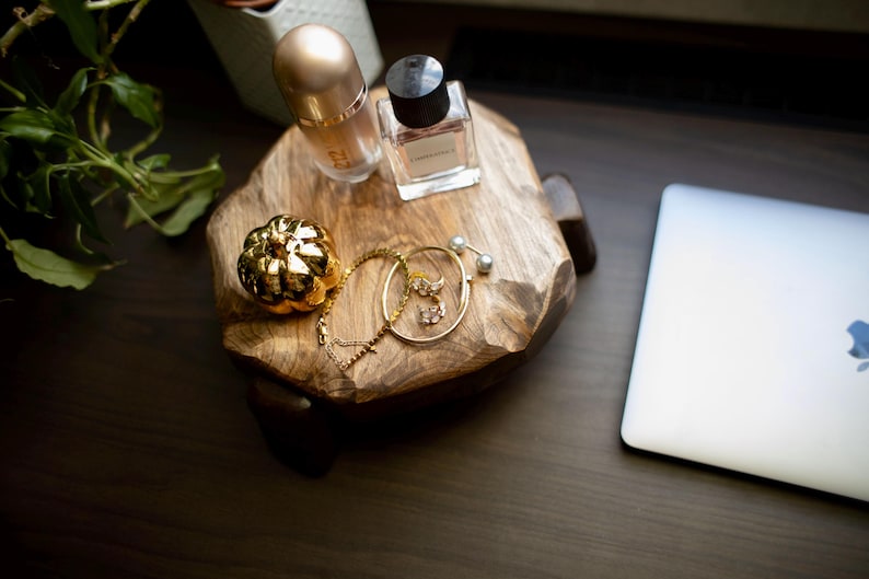 Puede incluir: Una bandeja decorativa de madera con un frasco de perfume dorado, un frasco de perfume peque&ntilde;o, una calabaza dorada y joyas doradas. Un port&aacute;til plateado est&aacute; a la derecha. Una planta est&aacute; en el fondo.
