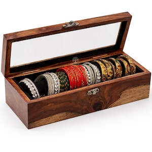 May include: A wooden jewelry box with a clear glass lid, open to reveal an assortment of bangles. The bangles are in various colors, including red, green, gold, and silver. The box is made of dark wood.