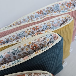 Peut inclure: Une collection de quatre trousses zippées en velours côtelé dans des tons rose poudré, jaune moutarde, bleu sarcelle foncé et terre cuite. Chaque trousse possède une fermeture éclair crème et une doublure intérieure à motif de petites fleurs.