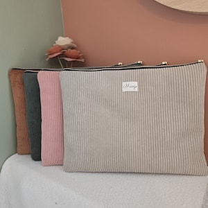Könnte beinhalten: Vier Cord-Reißverschlusstaschen in Braun, Grün, Rosa und Beige. Die beige Tasche hat ein kleines weißes Etikett mit dem Namen "Maanja". Die Taschen liegen auf einer weißen Oberfläche.