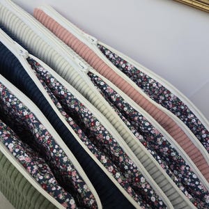 Peut inclure: Plusieurs pochettes en velours côtelé zippées, de couleurs variées : vert olive, bleu marine et rose. Chaque pochette est doublée d'un tissu à motifs floraux et possède une fermeture éclair blanche. Disposition en angle.