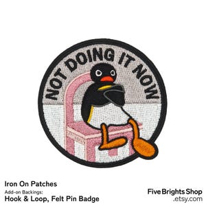 Op de afbeelding: Ronde geborduurde patch met een zwarte rand, met een cartoonpinguïn op een roze stoel. De tekst "NOT DOING IT NOW" staat in een cirkelvormig ontwerp. De patch is zwart, wit, oranje en roze.