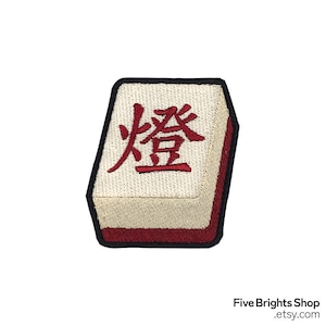 May include: Embroidered patch featuring a Mahjong tile with the Chinese character for "light" or "lamp" in red. The tile has a beige background, a black border, and a red edge.