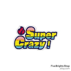 Op de afbeelding: Een kleurrijke geborduurde patch met de woorden "Super Crazy!" in geel, blauw en roze, omlijnd in blauw. Een rode vlammenafbeelding staat aan de linkerkant. De patch staat op een witte achtergrond.