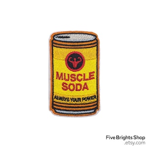 Könnte beinhalten: Gestickter Aufnäher in Form einer Getränkedose. Die Dose ist gelb mit den roten Worten "MUSCLE SODA" und einem roten Muskelsymbol. Der Text "ALWAYS YOUR POWER" steht unten. Der Aufnäher hat einen schwarzen Rand.