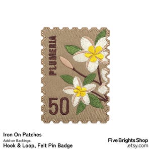 Könnte beinhalten: Gestickter Aufnäher in Form einer Briefmarke mit Plumeria-Blüten. Der Aufnäher ist beige mit weißen und gelben Blüten, grünen Blättern und der Zahl 50. Das Wort "PLUMERIA" ist vertikal aufgedruckt.