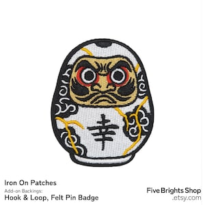 May include: Embroidered Daruma doll patch with a white body, black accents, and a stern face with red eyes. The patch features the Japanese character for "happiness" and yellow stitching details. This iron-on patch is a unique accessory.