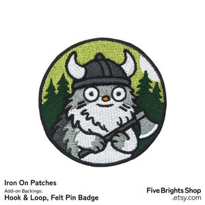 Peut inclure: Écusson rond brodé représentant un personnage de dessin animé portant un casque viking et tenant une hache. Le personnage est gris et blanc, sur un fond vert et blanc avec des pins. Le texte comprend "Iron On Patches" et "Hook & Loop, Felt Pin Badge".