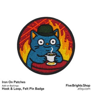 May include: Circular embroidered patch with a blue cat in a bowler hat, sipping coffee, set against a fiery background. The patch has a red border and the text "Iron On Patches" is visible.