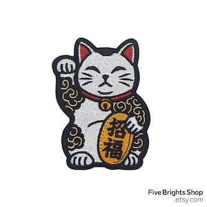May include: Embroidered patch featuring a white Maneki-neko cat with a raised paw, a red collar, and a gold coin. The cat is outlined in black with gold scrollwork. The coin has gold Japanese characters. The patch is a symbol of good luck.