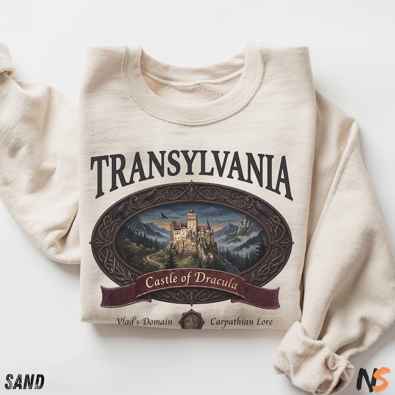 Puede incluir: Una sudadera de cuello redondo color arena con un estampado gr&aacute;fico que incluye el texto TRANSYLVANIA, Castle of Dracula, Vlad's Domain y Carpathian Lore. El dise&ntilde;o presenta un marco ovalado que rodea un castillo.