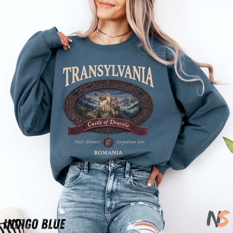 Puede incluir: Una sudadera de cuello redondo color azul &iacute;ndigo con un estampado gr&aacute;fico que incluye el texto TRANSYLVANIA, Castle of Dracula, Vlad's Domain, Carpathian Lore y ROMANIA. El dise&ntilde;o presenta un marco ovalado que rodea una ilustraci&oacute;n detallada de un castillo.
