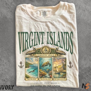 May include: Ivory-colored t-shirt with a green graphic that reads "VIRGIN ISLANDS." The graphic includes illustrations of pelicans, a compass, and three scenic views of the islands. The text "EXPLORE SWIM RELAX" is also printed on the shirt.