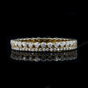 Könnte beinhalten: Ein goldener Bandring mit zwei Reihen kleiner, runder, klarer Edelsteine. Der Ring ist vor einem schwarzen Hintergrund platziert, und seine Reflexion ist darunter sichtbar. Der Ring scheint ein Ehering oder ein Eternity-Ring zu sein.