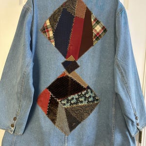 May include: Light blue denim jacket with patchwork diamond designs on the back. The patchwork includes various fabrics in red, brown, navy, and patterned textiles. The collar and hem are trimmed with yellow fringe.