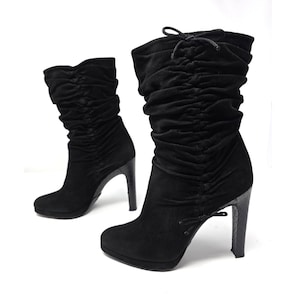 May include: A pair of black mid-calf boots featuring a soft, ruched upper material with a drawstring tie at the top and bottom. The boots have a rounded toe, a platform sole, and a high, textured stiletto heel. The design is consistent across both.