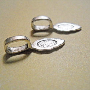 May include: Two silver-toned metal pendant bails with a teardrop shape and a small loop at the top. The bails are designed to be used for attaching pendants to necklaces or bracelets.