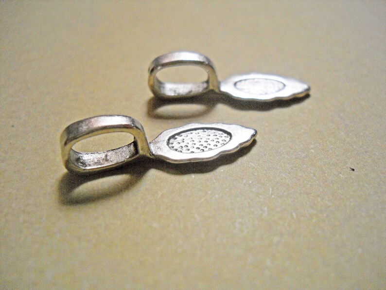 May include: Two silver-toned metal pendant bails with a teardrop shape and a small loop at the top. The bails are designed to be used for attaching pendants to necklaces or bracelets.