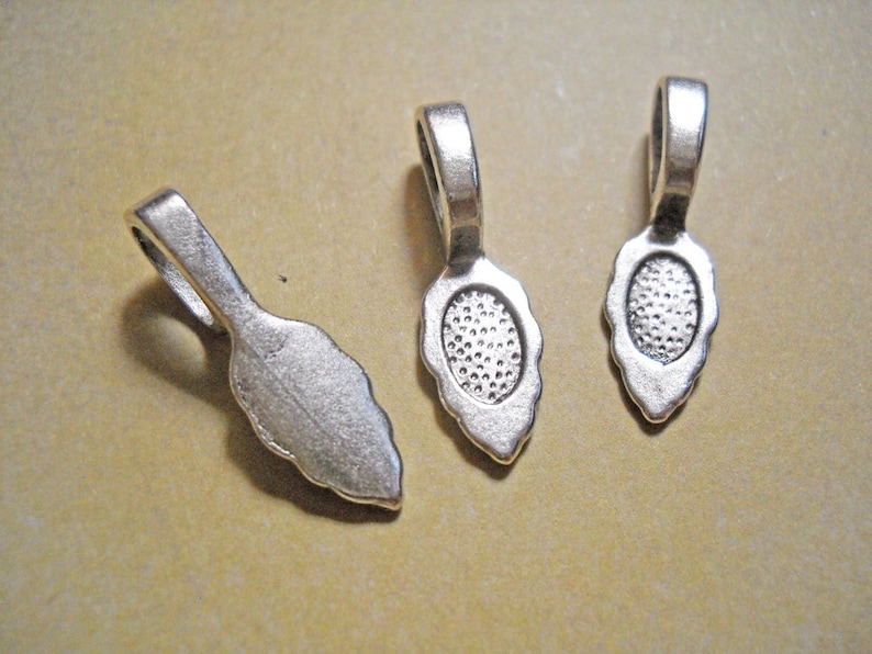 May include: Three silver-toned metal pendant bails with a teardrop shape and a loop at the top. The bails have a textured surface.