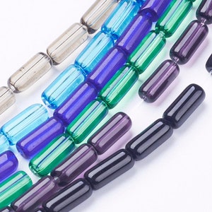 Puede incluir: Primer plano de una hebra de cuentas de vidrio en varios colores, incluyendo transparente, azul, verde y morado. Las cuentas son de forma cilíndrica y tienen un acabado liso y pulido.