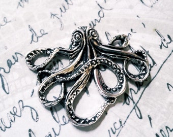 May include: A silver octopus charm with detailed tentacles and a textured surface. The charm is on a white background with handwritten text.