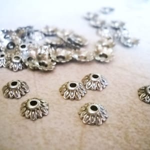 May include: Silver metal bead caps with a decorative, scalloped edge. The caps have a small hole in the center for threading.