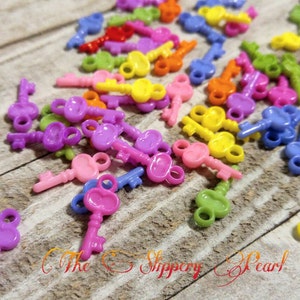 May include: A large pile of colorful plastic key charms in various shades of purple, pink, yellow, orange, and green. The keys are scattered on a wooden surface.
