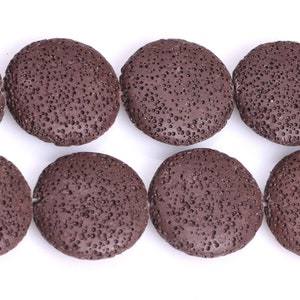 May include: Close-up of several dark brown, porous, round lava rock beads. The beads are flat and have a textured surface with many small holes. They are strung together on a white background, ideal for jewelry making.