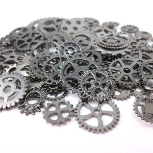May include: A collection of small, metallic gray gears of various sizes and designs. The gears are scattered, with some overlapping, creating a textured, mechanical aesthetic. The gears have a dark, gunmetal finish and are set against a white background.