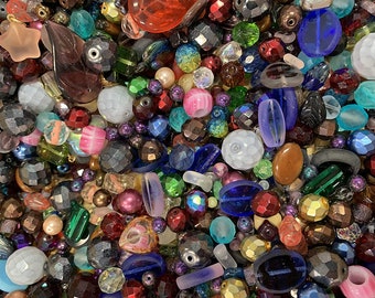 May include: A large assortment of colorful glass beads in various shapes and sizes. The beads are a mix of opaque and transparent colors, including red, blue, green, purple, and white.