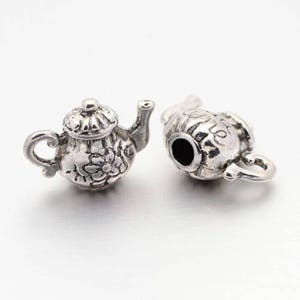 Peut inclure: Deux breloques en forme de théière argentées avec des motifs floraux complexes. Les breloques sont détaillées et ont une esthétique vintage.