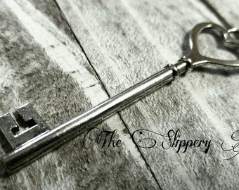May include: A silver key with a heart-shaped bow at the top. The key is lying on a wooden surface.
