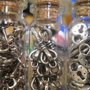 May include: Three glass bottles filled with silver-toned keys and lock charms. The bottles have cork tops and are clear glass.