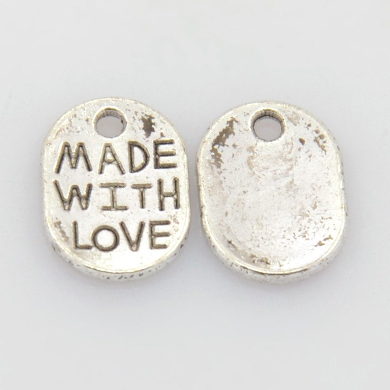 May include: Two silver oval-shaped metal charms with a hole at the top for hanging. One charm has the words "MADE WITH LOVE" engraved on it.