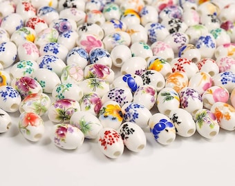 May include: A collection of white ceramic oval beads with colorful floral designs. The beads are perfect for jewelry making, crafting, and home decor.