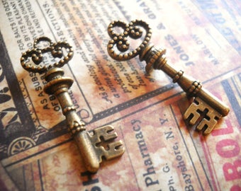 May include: Two antique-style skeleton keys with ornate designs. The keys are made of metal and have a bronze finish. The keys are lying on a piece of paper with text.