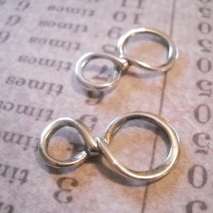 May include: Two silver infinity symbol charms, each with a smooth, rounded finish. The charms are linked together, creating a continuous loop.