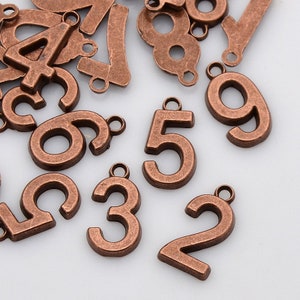 May include: A collection of antique copper-toned metal number charms. The numbers range from 0 to 9 and have a distressed finish.