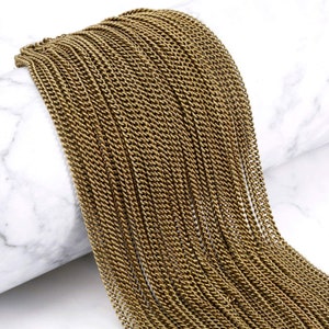 May include: A close-up of a gold-colored chain, made of many small, linked pieces. The chain is lying on a white surface.