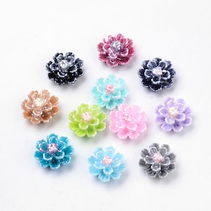 May include: Assortment of 10 flower-shaped resin embellishments in various colors, including pink, blue, green, purple, and brown. Each flower has a pearl-like center.