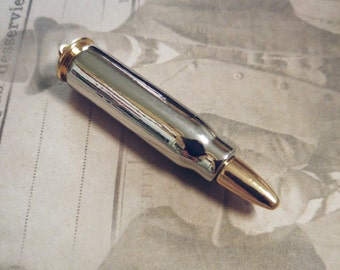 Könnte beinhalten: Ein silberner und goldener kugelförmiger Stift mit einer goldenen Spitze. Der Stift liegt auf einem Blatt Papier mit Schrift darauf.