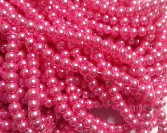 May include: Close-up of multiple strands of bright pink, round beads. The beads are tightly strung together, creating a dense, textured appearance. The beads have a glossy finish, reflecting light and adding to their vibrant color.