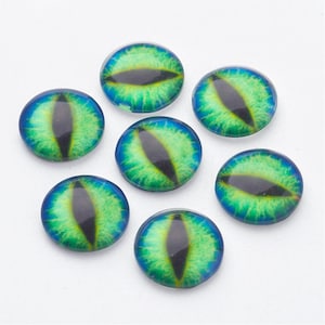 May include: Seven glass cabochons with a green and blue eye design. Each round cabochon features a black, oval-shaped pupil surrounded by shades of green and blue, creating a striking, reptilian eye effect. These are ideal for crafting.